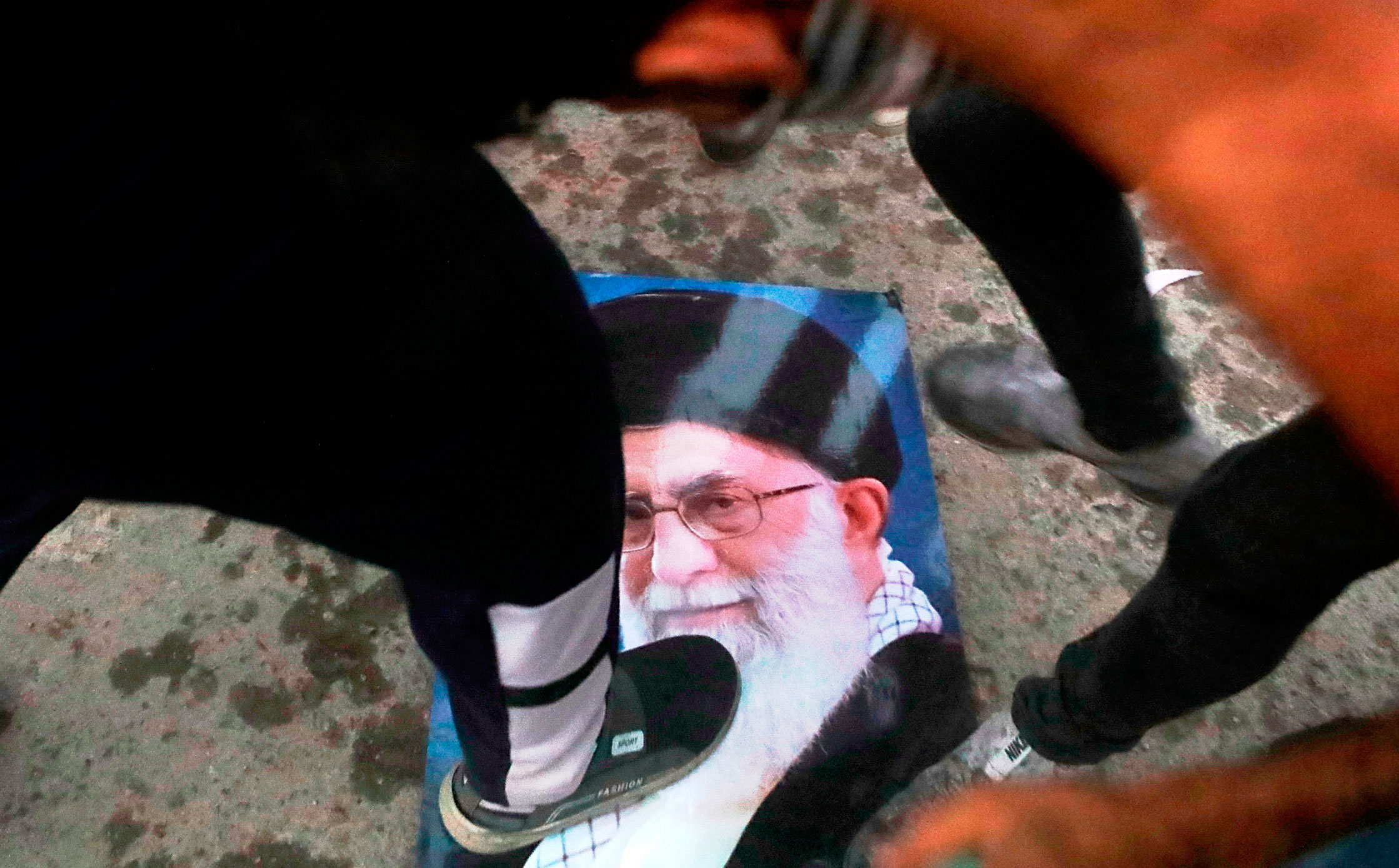محتج عراقي يدوس صورة علي خامنئي مرشد الثورة الإيرانية بعد حرق قنصلية إيران في البصرة