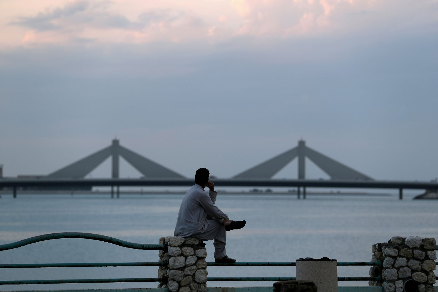 A man sits and looks towards the Sheikh Isa Causeway, linking Diplomatic Area to Muharraq, during the early evening hours in Manama, Bahrain, November 11, 2018.