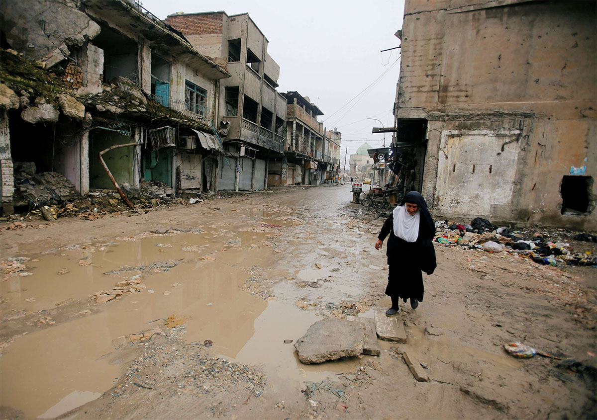 A woman walks next to damaged shops in the Old City of Mosul