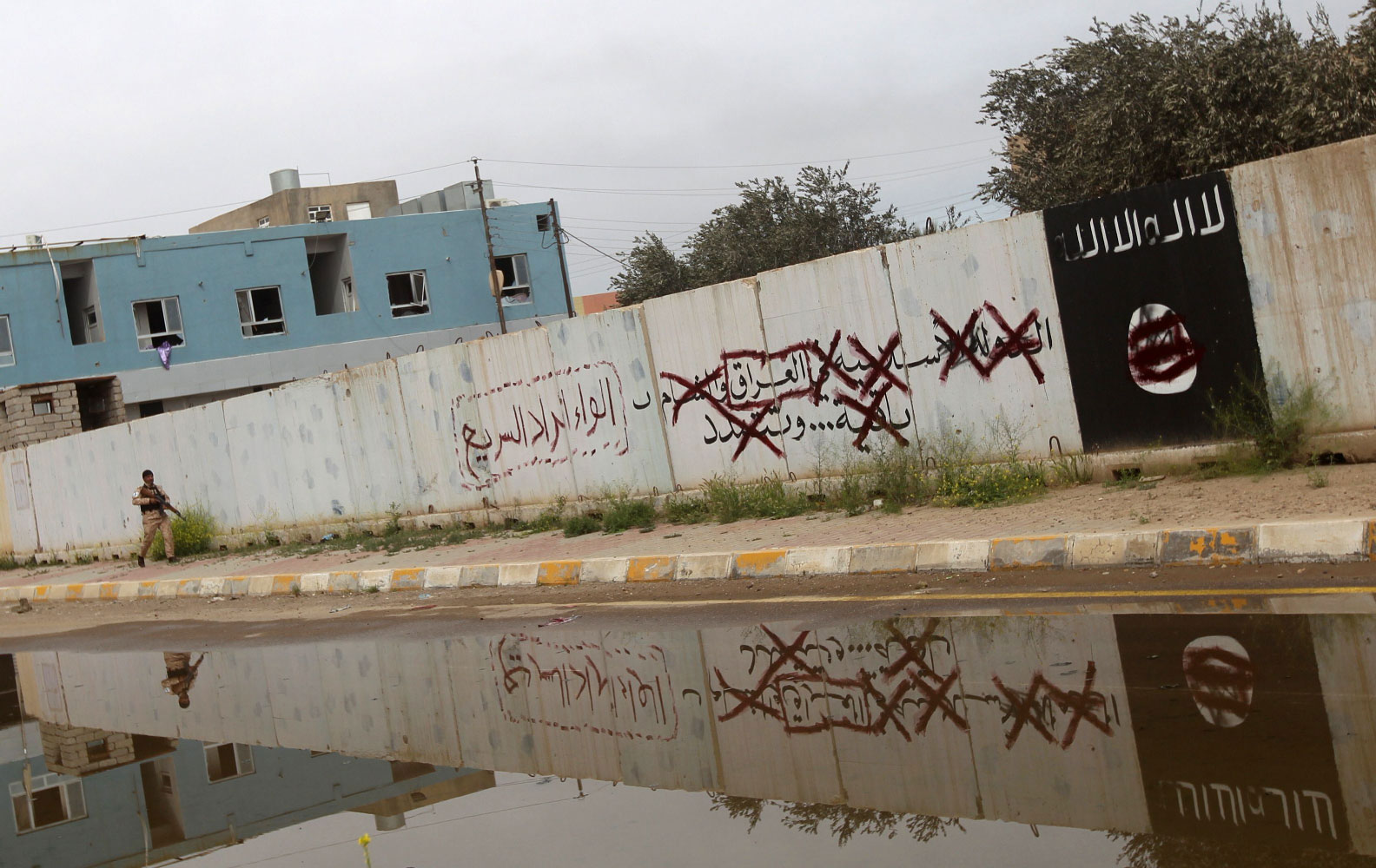 A Shiite fighter from the Popular Mobilisation units walks down an alley bearing defaced Islamist slogans and emblems in Tikrit on April 1, 2015.