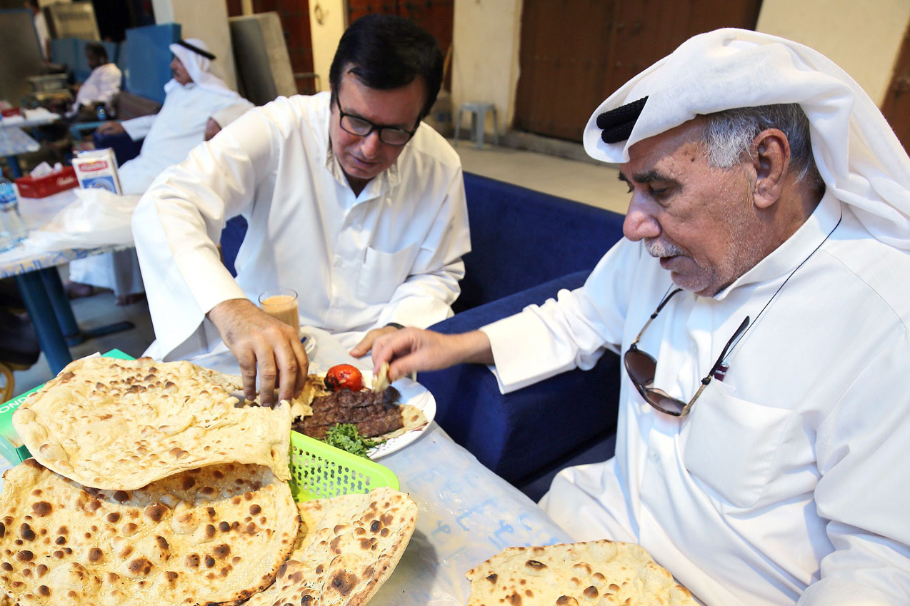 Hassan Abdullah Zachriaa, a Kuwaiti of Iranian origin and owner of the Al-Walimah restaurant, shares Iranian bread - known as taftoon - during a meal with a friend in Kuwait City