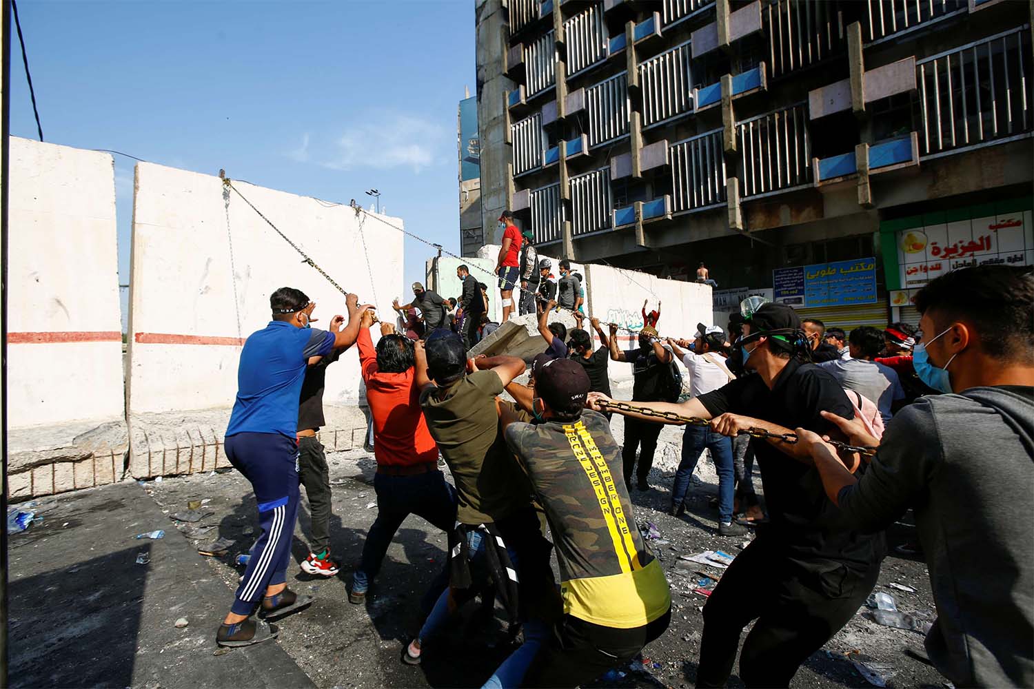 Iraqi demonstrators try to push down a concrete wall during ongoing anti-government protests in Baghdad