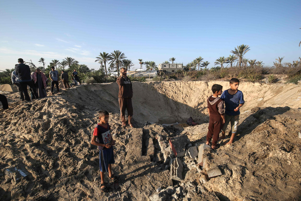Palestinian children stand around a crater caused by an Israeli airstrike