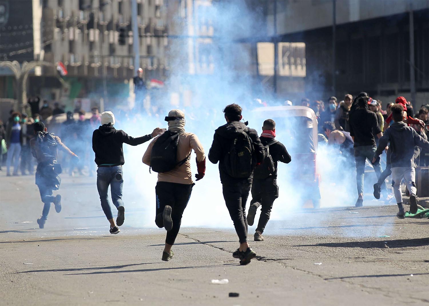 Iraqi protesters rush to catch a tear gas canisters fired by security forces during clashes following an anti-government protest in Baghdad