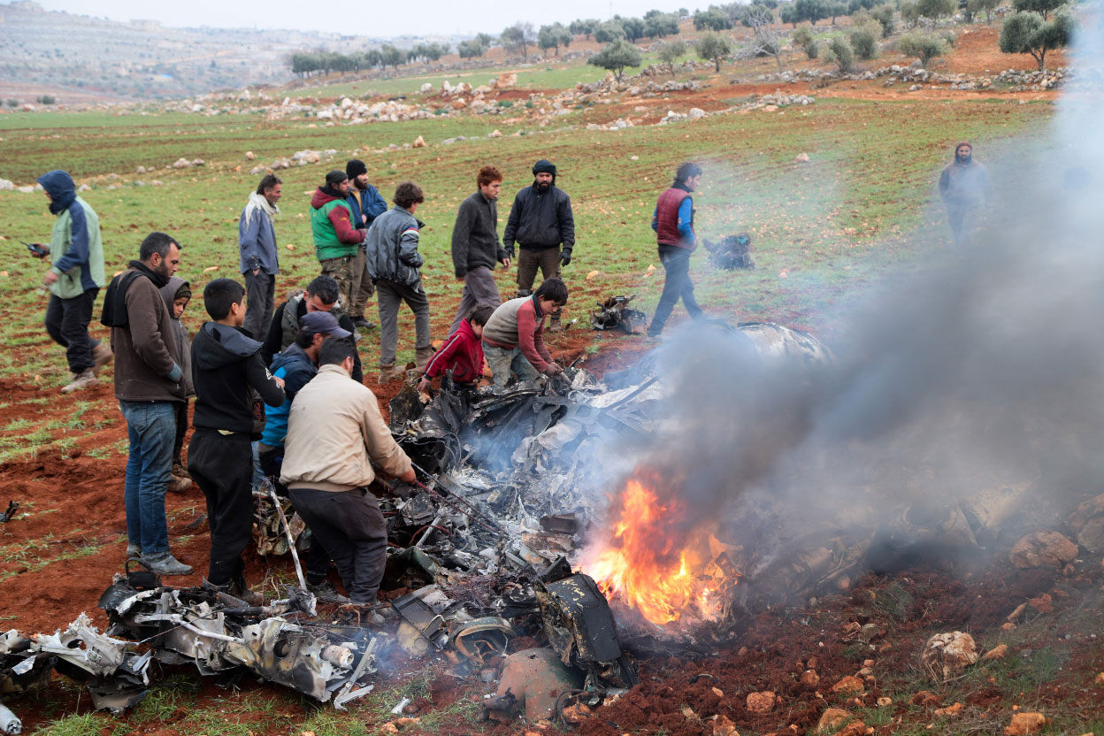 People inspect the wreckage of a military helicopter of the Syrian government forces that was downed over the western Aleppo Province