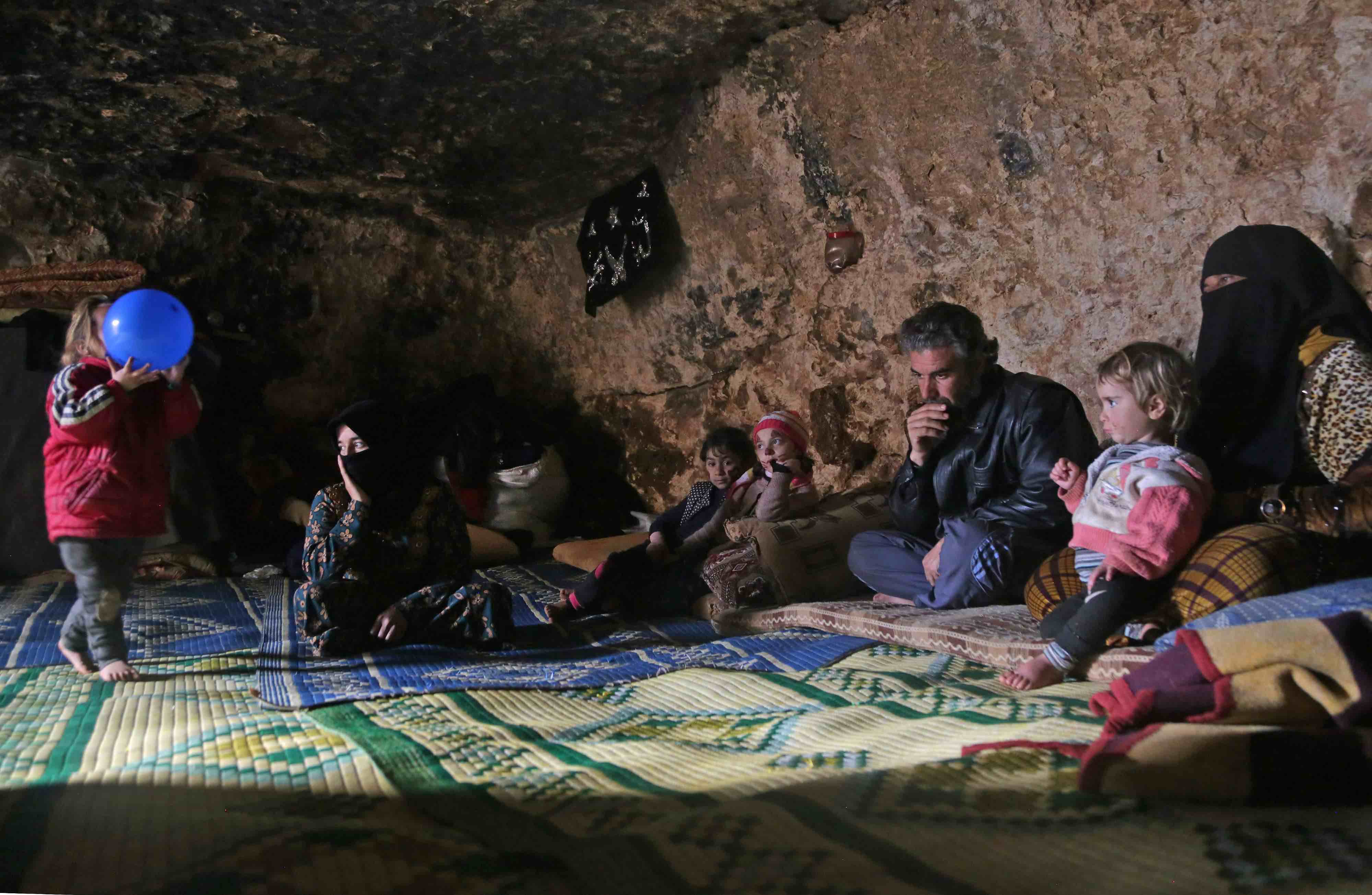 Darra's children huddle on a carpet around a tray covered in small bowls of hummus and dried oregano