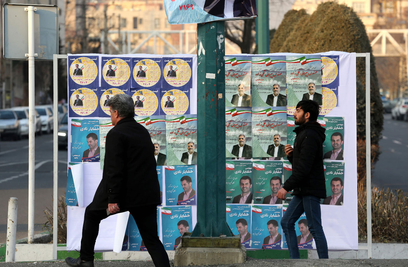 Iranians walk past electoral poster in a street of the capital Tehran