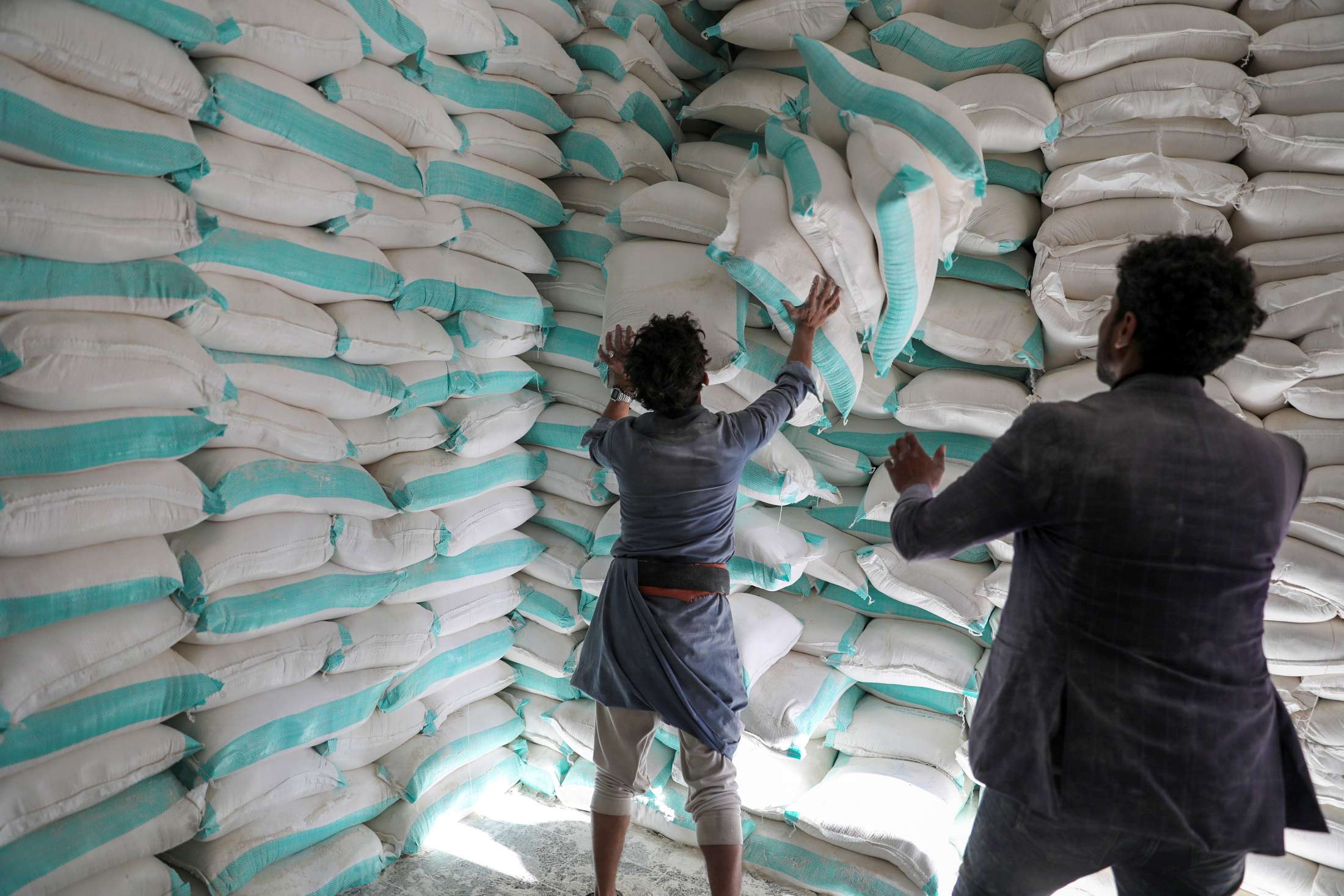 Workers handle sacks of wheat flour at a World Food Programme food aid distribution center in Sanaa