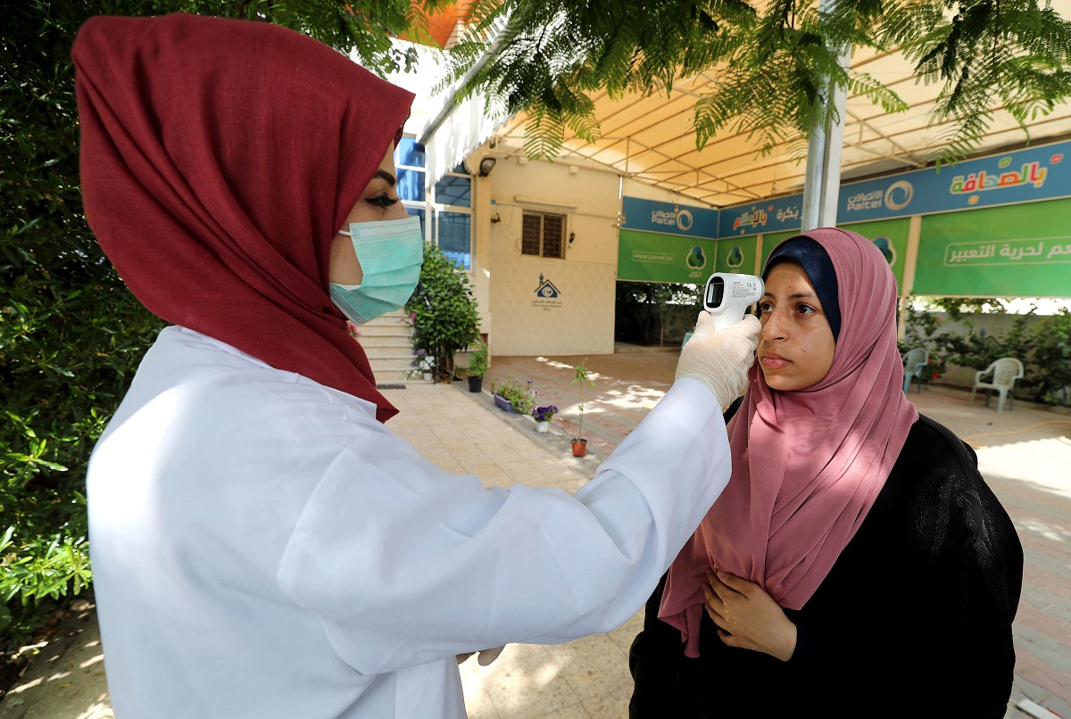 عاملة في مجال الرعاية الصحية تتحقق من درجة حرارة امرأة فلسطينية