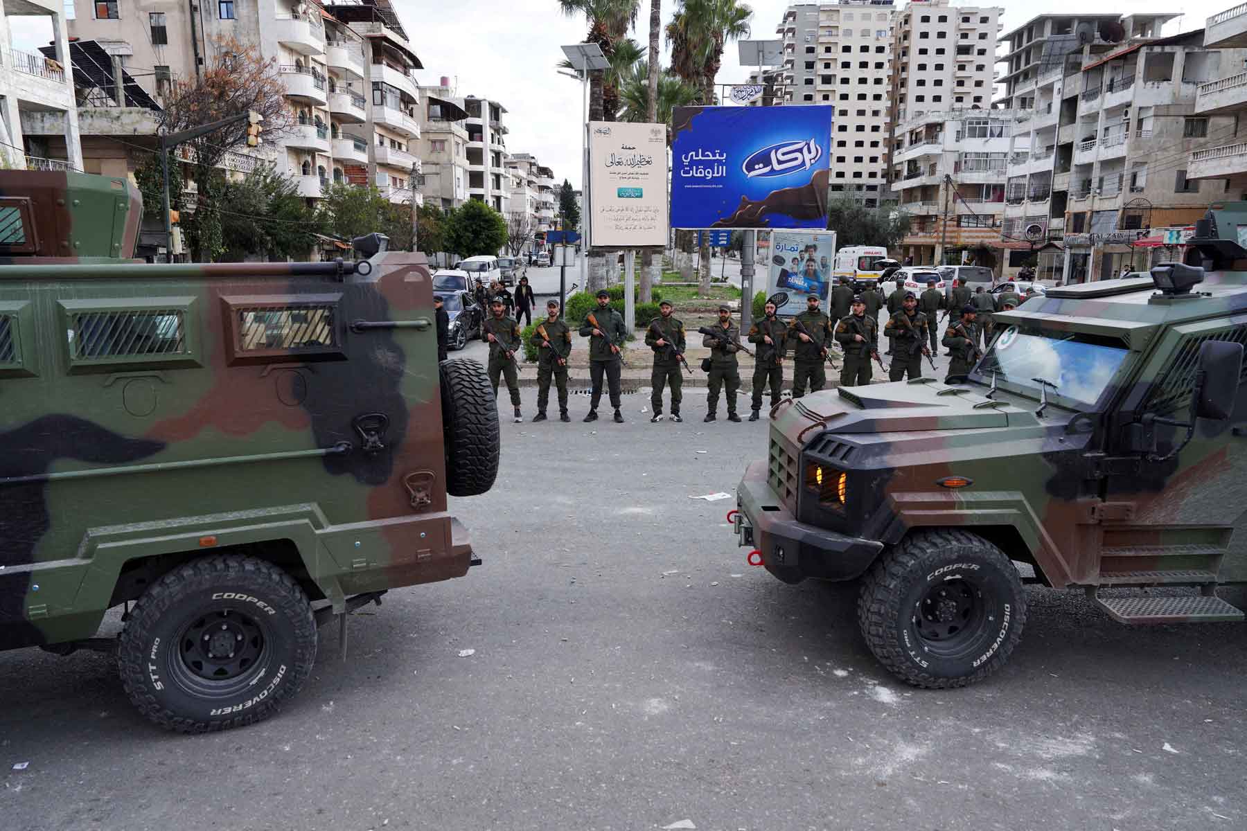Members of the Syrian Security forces stand guard near military vehicles on the day people from the Alawite sect protest as they demand federalism, in Latakia, Syria, December 28, 2025. 