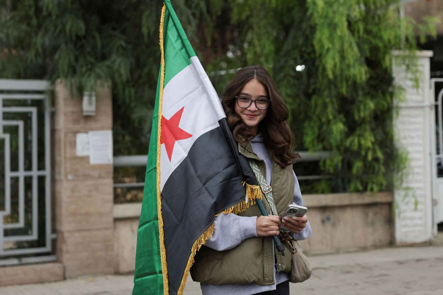 A woman holds a flag on the day of a military parade as Syrians mark the first anniversary of Bashar al-Assad’s fall, in Damascus, December 8, 2025. 