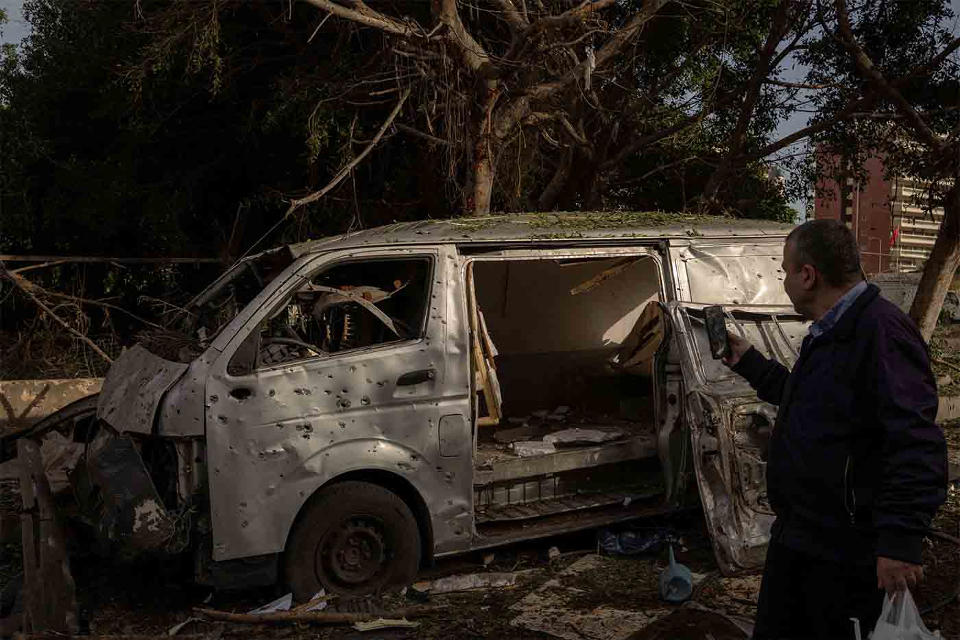A man takes a photo of a damaged car following an Israeli strike on Beirut