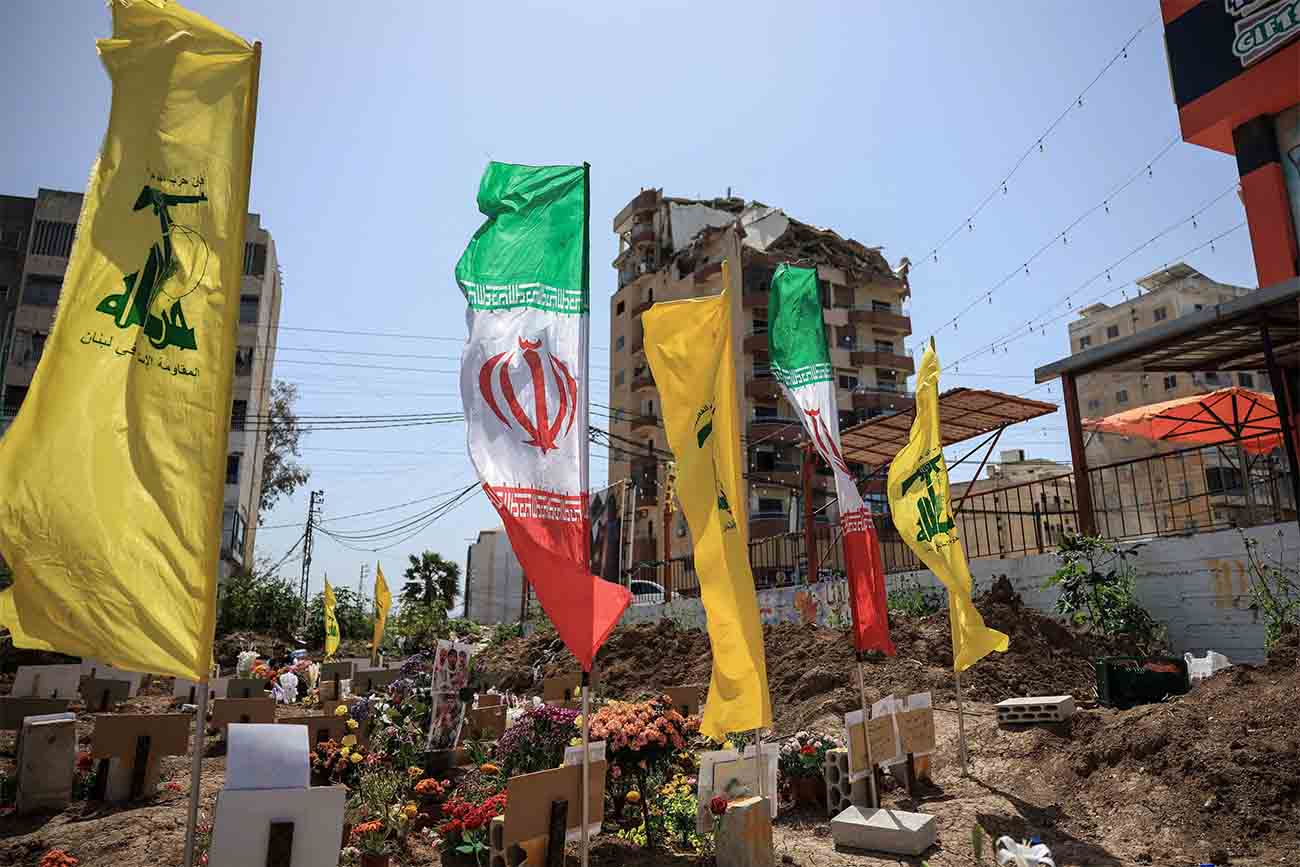 Hezbollah and Iranian flags flutter at a temporary graveyard by a damaged building in Tyre, south Lebanon