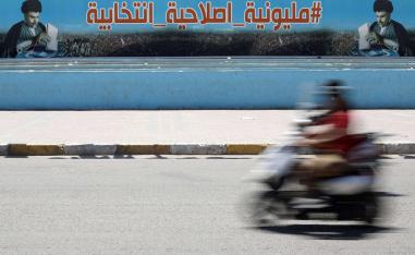 عراقي على دراجة يمر بجانب ملصق انتخابي لكتلة الصدر