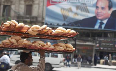 عامل يحمل خبزا يمر بالقرب من ملصق للرئيس المصري