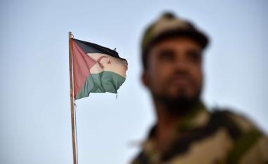 Uniformed soldiers of the pro-independence Polisario Front stand before a Sahrawi flag.