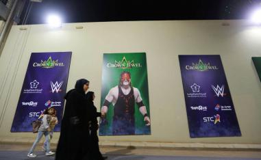 سعوديات يمررن بجانب ملصقات تعلن عن مسابقات للمصارعة الحرة