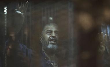 Egyptian Muslim Brotherhood financier Khairat al-Shater gestures from behind the defendant's cage as he attends his trial in Cairo on June 16, 2015. 
