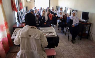 Smiling and tapping on their desks, a class of bright-eyed students sing, in English, "My face, my face, this is my nose".