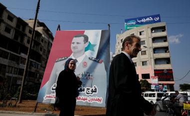 People walk in front of a billboard with a picture of Syrian President Bashar al-Assad in Homs, Syria, September 18, 2018.
