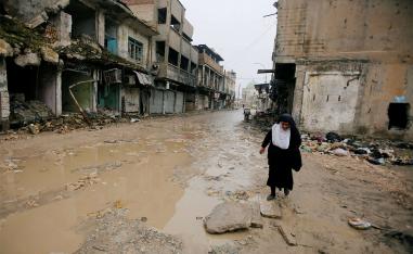 A woman walks next to damaged shops in the Old City of Mosul