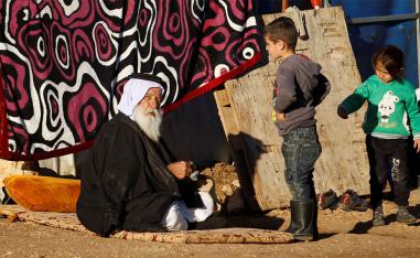 A man sits outside his tent as children look on at a refugee camp in Sinjar