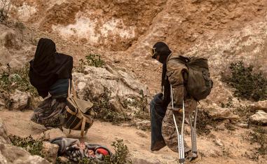 A man limps on crutches behind a woman as they walk with others said to be IS members