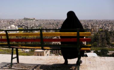 A woman sits on a bench overlooking Aleppo's ancient citadel and the old city