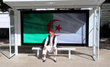 A man sits at a bus station decorated with the national flag in Algiers