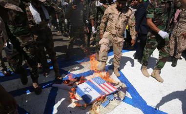 Iraqi Shiite fighters from the Iran-backed armed group, Hezbollah brigades, burn US and Israeli flags