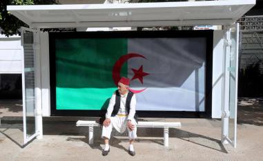 A man sits at a bus station decorated with the national flag during a protest demanding the removal of Algeria’s ruling elite in Algiers