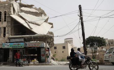 A man drives his motorcycle past a damaged building in the town of Binnish