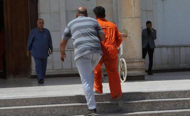 An Islamic State suspect wearing a red prison suit is led to the Iraqi Criminal Court in Baghdad