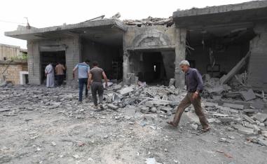 People walk past destruction at the scene of an area targeted by regime airstrikes