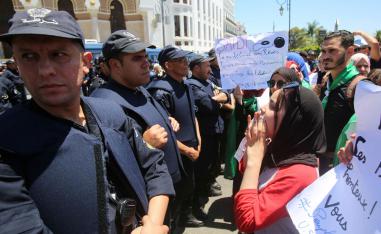 Police officers stand guard as students chant slogans during a protest demanding the removal of the ruling elite in Algiers