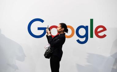 امرأة تلتقط صورة ذاتية بهاتفين أمام شعار غوغل خلال معرض للالكترونيات في باريس