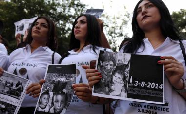Iraqi Yazidi women hold placards with pictures of victims of the 2014 invasion of their region by the Islamic State
