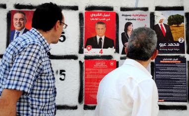 Men watch a campaign poster of the owner of the Tunisian private channel Nessma TV, Nabil Karoui (C)