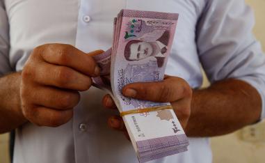 A Jordanian money changer holds Syrian currency