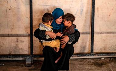 Volunteer caring for children linked with foreign fighters of the Islamic State, holds two at a camp in the village of Ain Issa