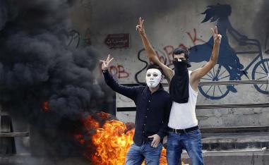 Anti-government protesters make victory signs next to tires that were set on fire to block a road during a demonstration, in Beirut