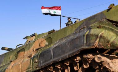 A Syrian soldier stands in a government forces' position near a deployed infantry-fighting vehicle