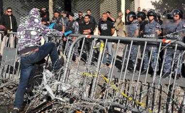 A Lebanese protester steps on a metal barrier through a barbed wire fence near the parliament headquarters in Beirut