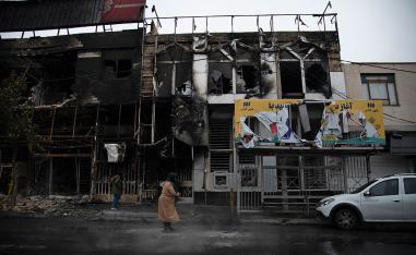 People walk past buildings which burned during protests in the city of Karaj, west of the capital Tehran
