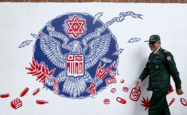 A member of Iran's Revolutionary Guards walks past a new mural painted on the walls of the formar US embassy in the capital Tehran