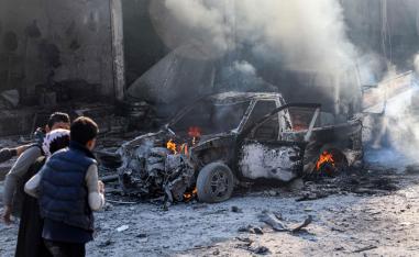 A woman is assisted as she walks past a burning car in Tal Abyad