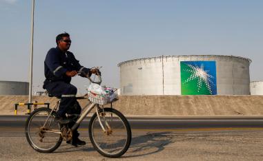 An employee rides a bicycle next to oil tanks at Saudi Aramco oil facility in Abqaiq