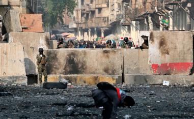 An anti-government protester picks up stones as security forces close Rasheed Street during protests in Baghdad