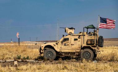 A US armoured vehicle drives past a burning gas flare from oil extraction
