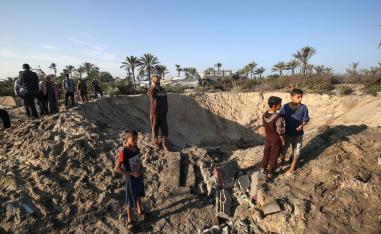 Palestinian children stand around a crater caused by an Israeli airstrike